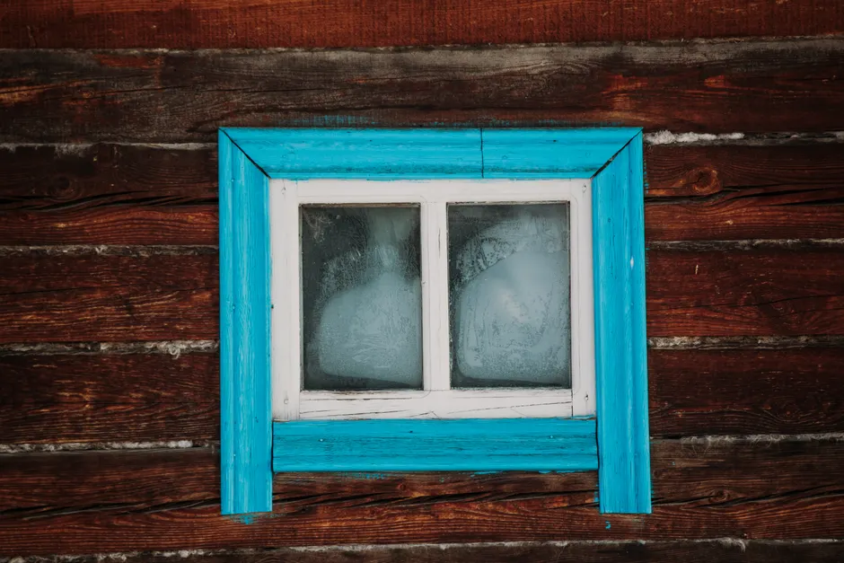 Close-up of a rustic wooden wall with a weathered blue-framed window.