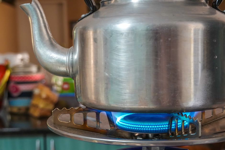 Close-up of a stainless steel kettle heating on a blue gas stove flame indoors.