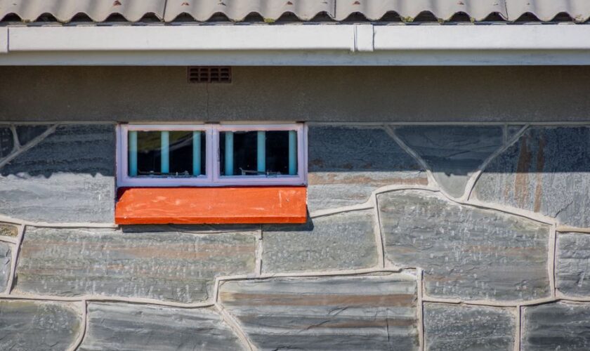 Close-up of a stone wall featuring a small window and orange sill, adding contrast to the rustic facade.