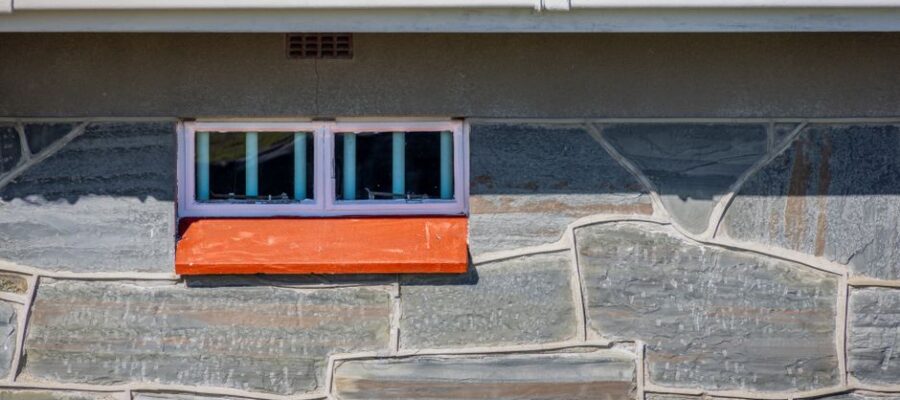 Close-up of a stone wall featuring a small window and orange sill, adding contrast to the rustic facade.