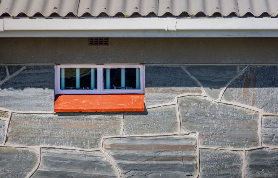 Close-up of a stone wall featuring a small window and orange sill, adding contrast to the rustic facade.
