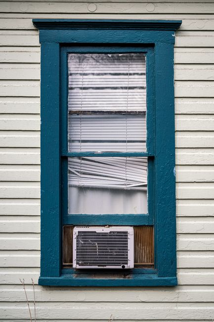 Close-up of a vintage wooden window with blue frame and air conditioner.