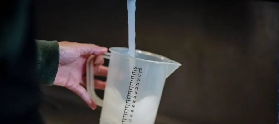 Close-up of hand holding measuring pitcher under a faucet with running water indoors.