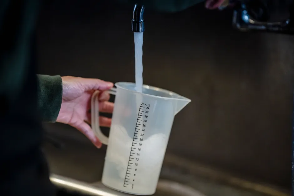Close-up of hand holding measuring pitcher under a faucet with running water indoors.