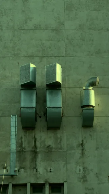 Close-up of industrial ventilation ducts on a city building wall.