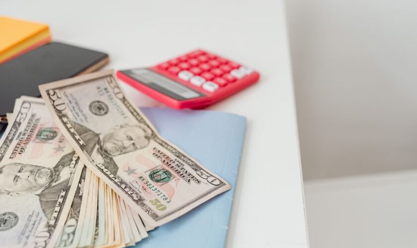 Close-up of notebooks, US dollars, and a calculator on a desk.