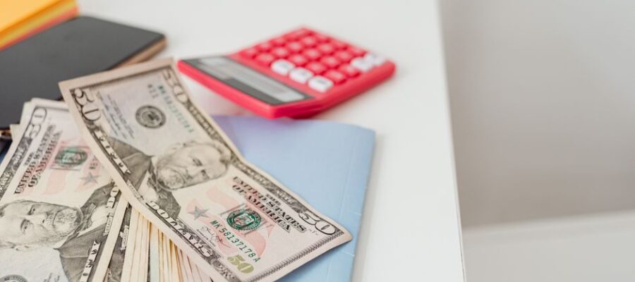 Close-up of notebooks, US dollars, and a calculator on a desk.