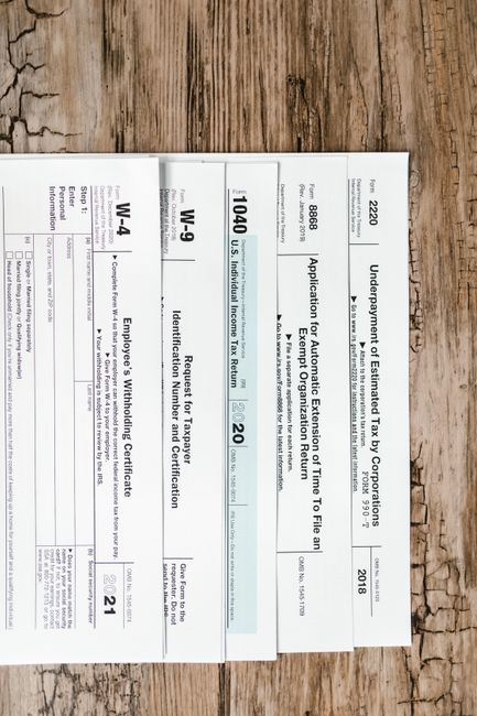 Close-up of various U.S. tax forms including W-4, W-9, and 1040 on a rustic wooden surface.