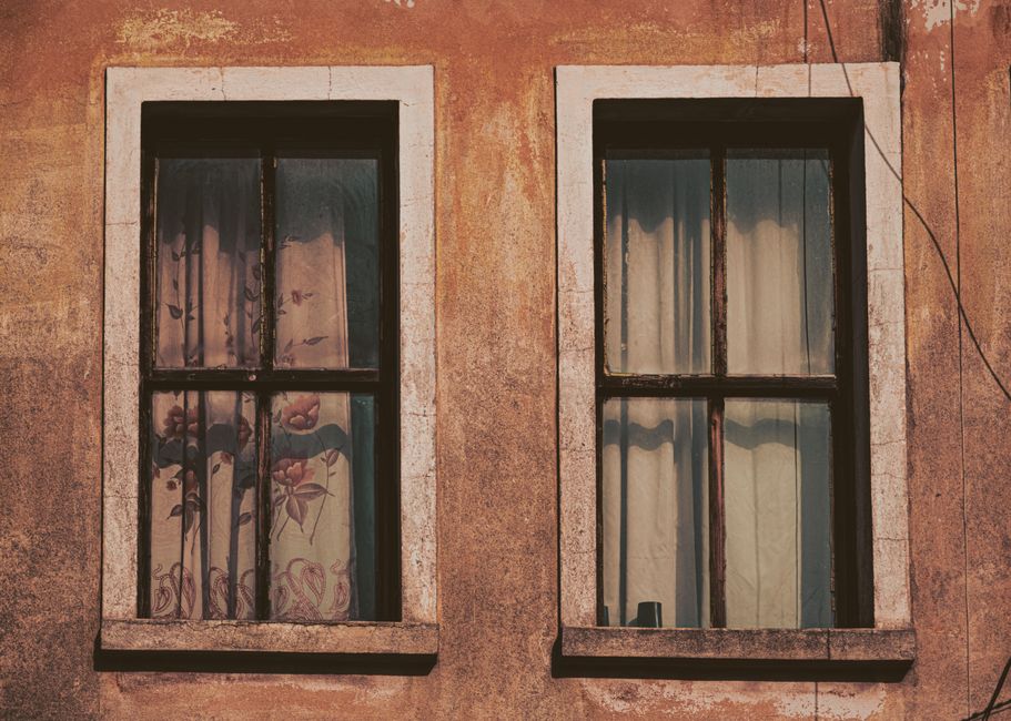 Close-up view of a rustic double window with floral curtains, showcasing aged elegance.