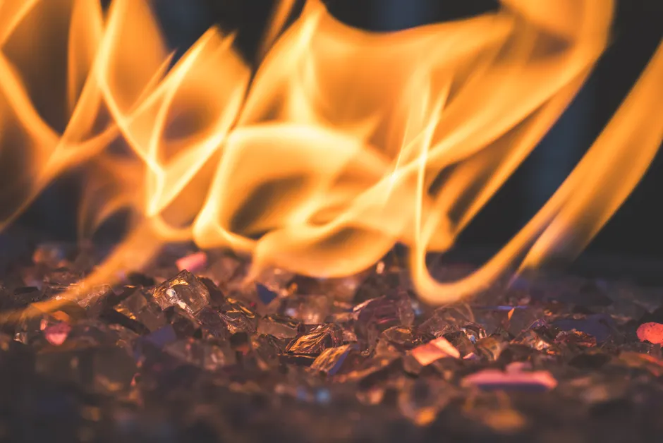 Closeup of warm, vibrant flames dancing over decorative glass rocks, creating a mesmerizing fire effect.