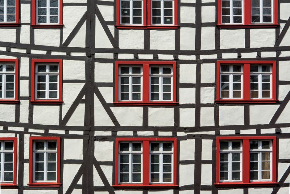 Detailed view of a half-timbered building facade featuring red window frames and geometric patterns.