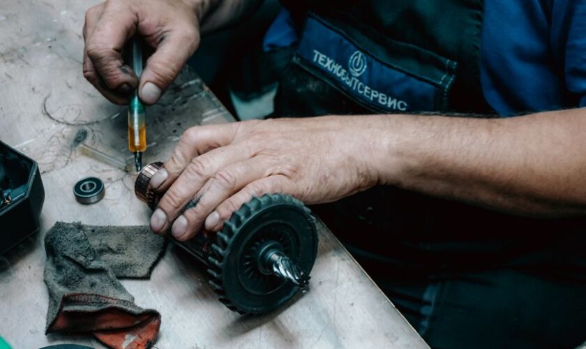 Detailed view of a technician working on a mechanical gear part with precision tools on a workbench.