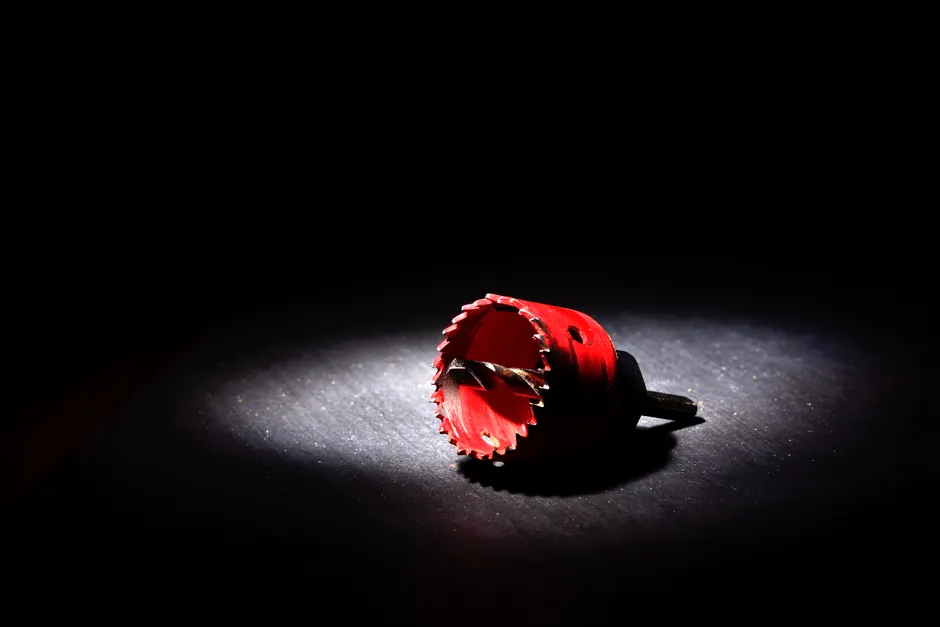 Dramatic shot of a red hole saw tool illuminated against a black background in studio lighting.