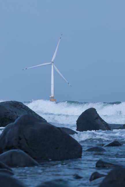 Dynamic scene showcasing an offshore wind turbine amidst ocean waves and rocky shoreline.