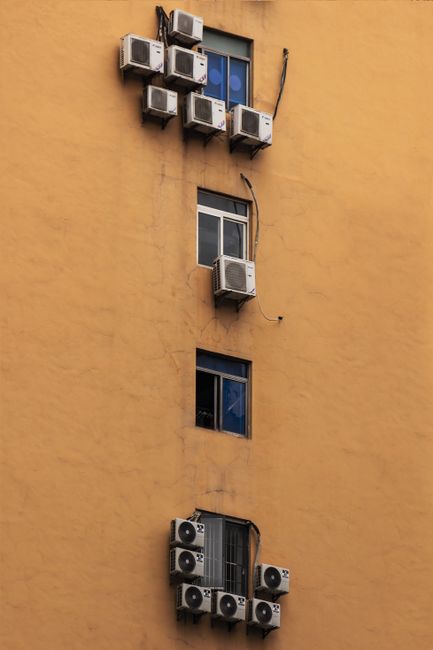 Facade of a building with numerous air conditioners installed on apartment windows.