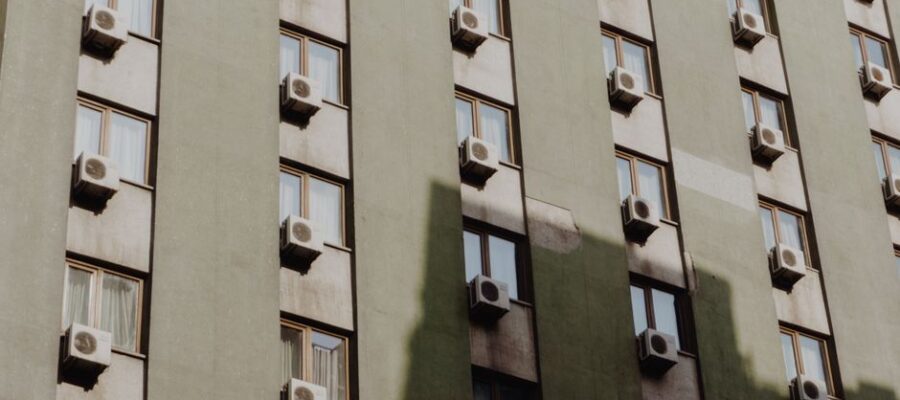 Facade of a city apartment building equipped with air conditioners on each window.
