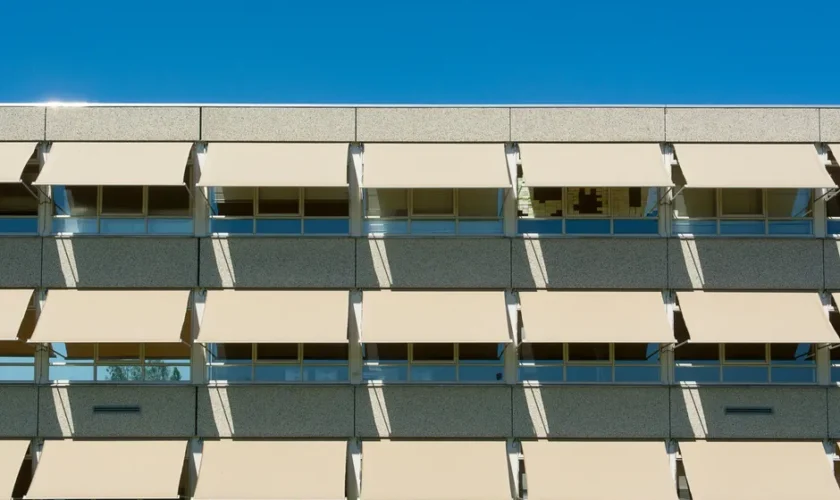 Facade of a modern residential building with sun shades under a clear blue sky.