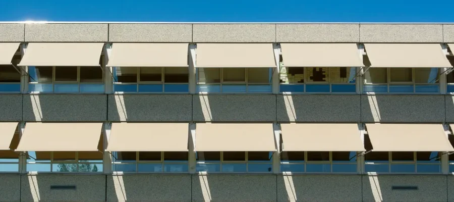 Facade of a modern residential building with sun shades under a clear blue sky.