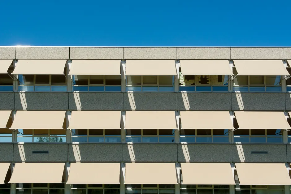 Facade of a modern residential building with sun shades under a clear blue sky.