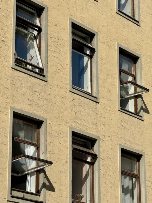 Facade of an apartment building in Oslo with open windows and sunlight casting shadows.