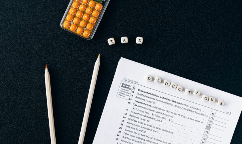 Flat lay of tax form, pencils, and calculator on black background, emphasizing tax deductions.