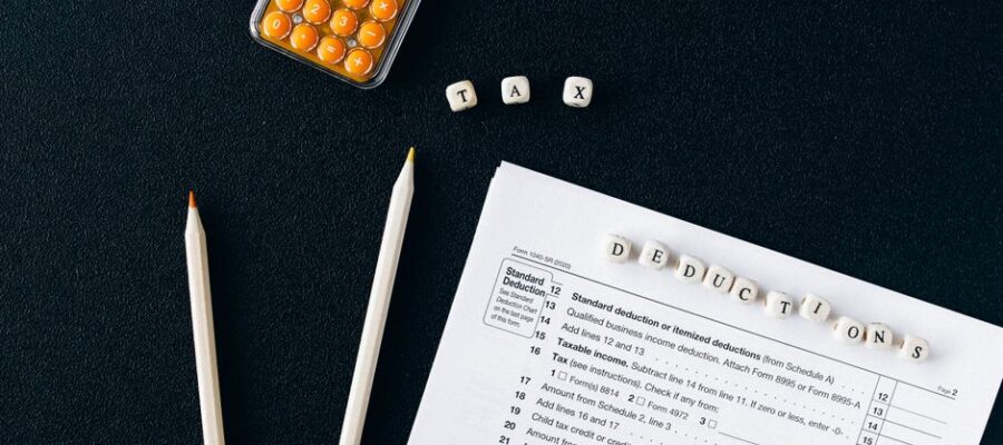 Flat lay of tax form, pencils, and calculator on black background, emphasizing tax deductions.