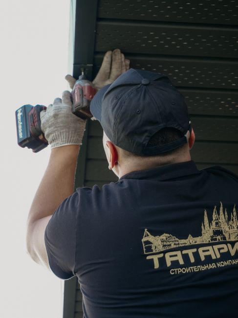 Focused construction worker installing roof siding with a drill outdoors.