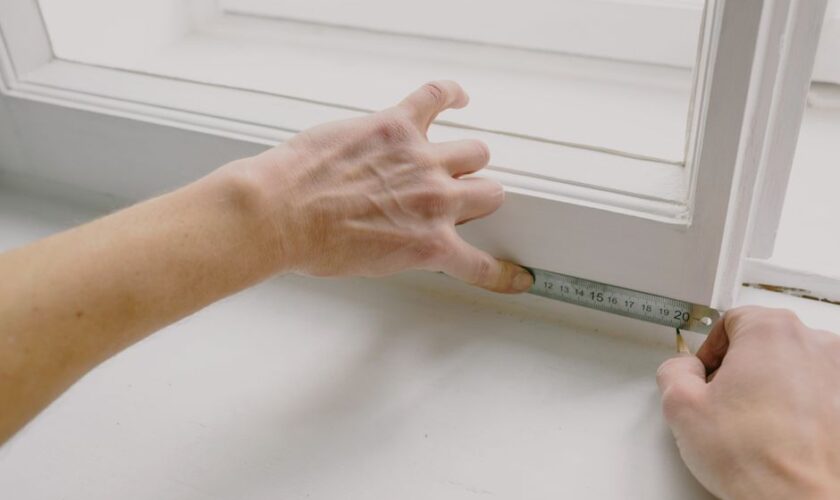 From above of crop anonymous workman measuring wooden window frame using metal ruler and pencil in house