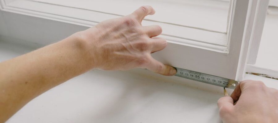 From above of crop anonymous workman measuring wooden window frame using metal ruler and pencil in house