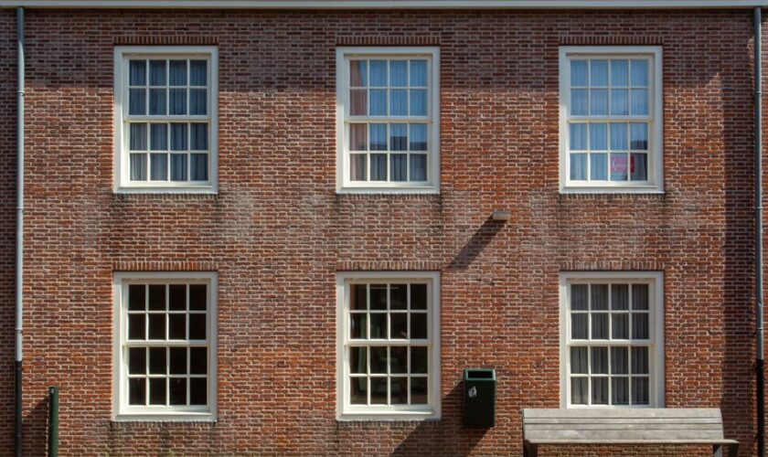 Front view of a brick building facade with sash windows and a wooden bench.