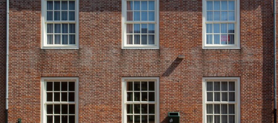 Front view of a brick building facade with sash windows and a wooden bench.