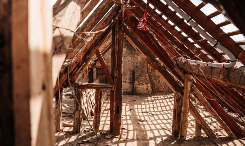 Interior view of wooden framing and rafters in a partially constructed attic space, highlighting a rustic and textured structure.