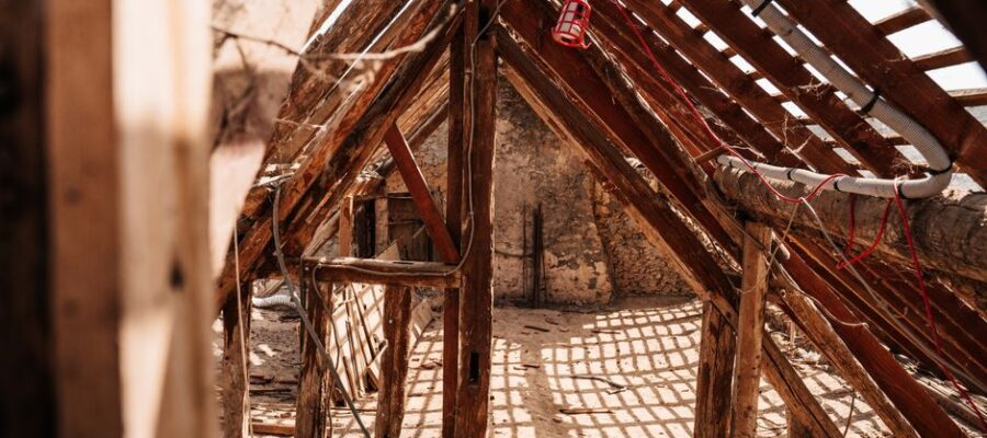 Interior view of wooden framing and rafters in a partially constructed attic space, highlighting a rustic and textured structure.