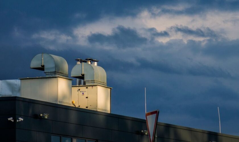 Low angle of metal pipes of ventilation system located on rooftop of industrial building against cloudy sky