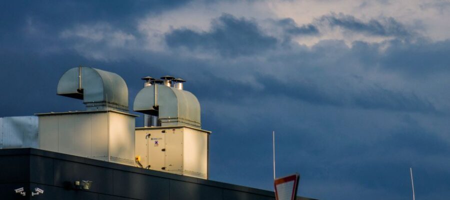 Low angle of metal pipes of ventilation system located on rooftop of industrial building against cloudy sky