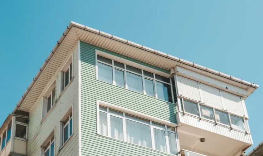 Low angle view of a modern apartment building exterior with glass windows under a clear blue sky.