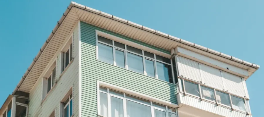 Low angle view of a modern apartment building exterior with glass windows under a clear blue sky.