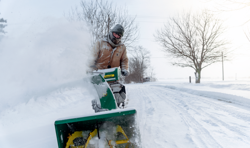 Man using a snow blower to clear snow during winter in Essex, ON under cold weather conditions.
