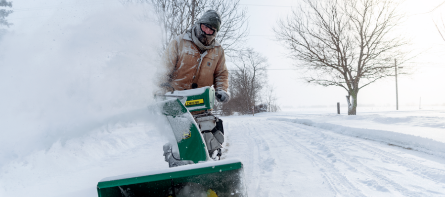 Man using a snow blower to clear snow during winter in Essex, ON under cold weather conditions.