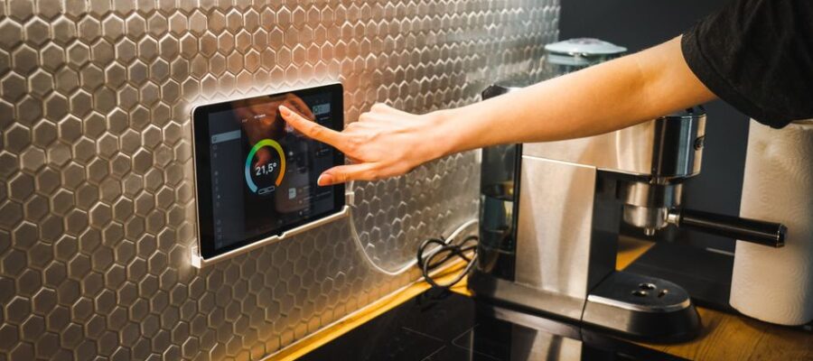 Modern kitchen scene featuring a hand using a tablet to control a smart home system.