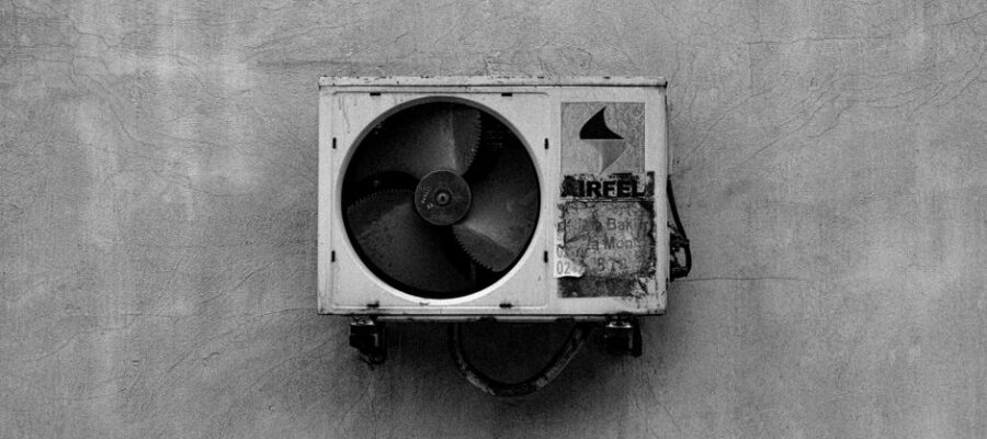 Monochrome image of a wall-mounted air conditioner on a concrete surface.