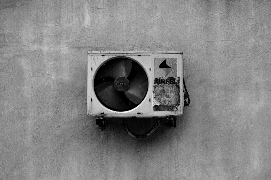 Monochrome image of a wall-mounted air conditioner on a concrete surface.