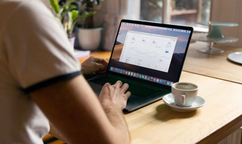 Person working on a laptop with analytics in a cozy home office setting, coffee in hand.
