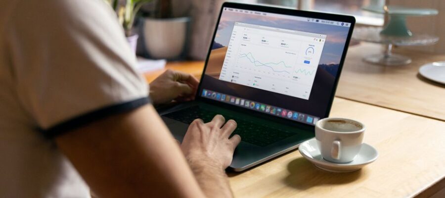 Person working on a laptop with analytics in a cozy home office setting, coffee in hand.
