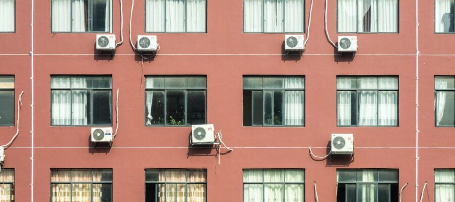 Red building exterior with multiple windows and air conditioners, showcasing urban architecture.