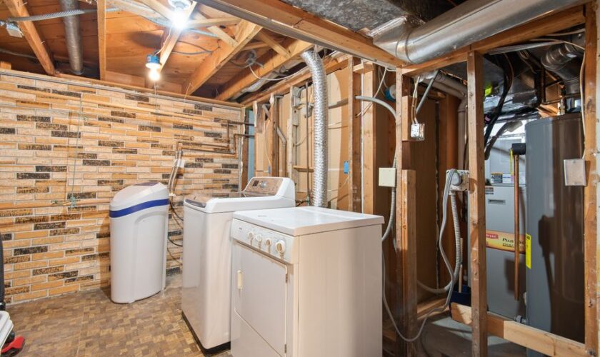 Spacious basement laundry room featuring modern appliances and exposed brickwork.