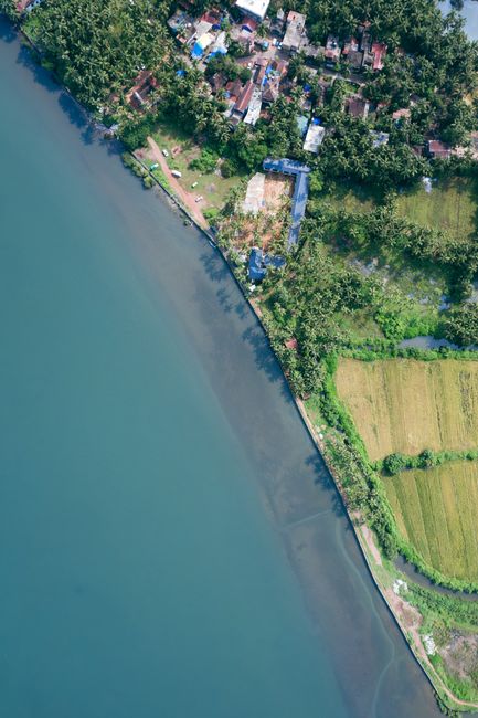Stunning aerial shot of a coastal village in Goa, India, with lush fields and a serene river.