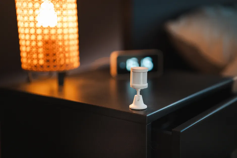Stylish bedroom with smart motion sensor, lamp, and alarm clock on wooden nightstand.