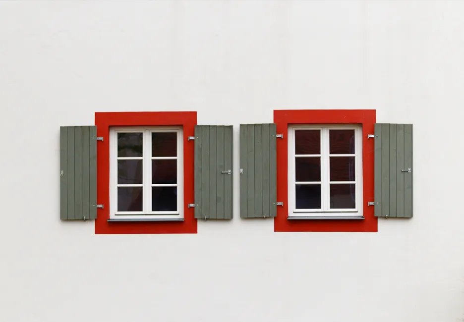 Symmetrical windows with red frames and green shutters on a white wall, minimalist design.