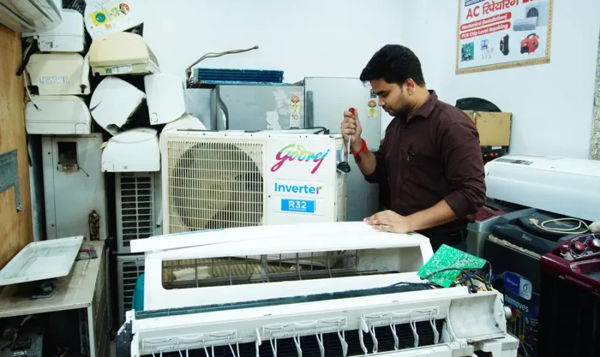 Technician repairing an air conditioner unit in New Delhi workshop.